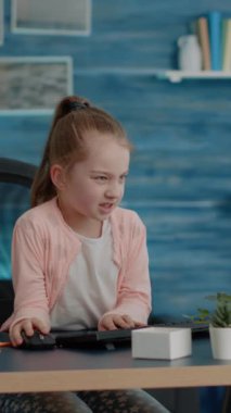 Dikey video: Hayal kırıklığına uğramış çocuk evden bilgisayarla çevrimiçi derslere katılıyor. Genç kız klavyeyle monitör kullanırken derslere ve ödevlere sinir oluyor. Yorgun kız.