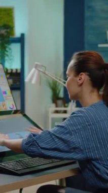 Dikey video: Ofis stüdyosundaki resimler üzerinde çalışan rötuş uzmanı. Grafik sanatçısı fotoğraf projesi için dokunmatik ekran ile monitörde rötuşlama yazılımı kullanıyor. Profesyonel medya