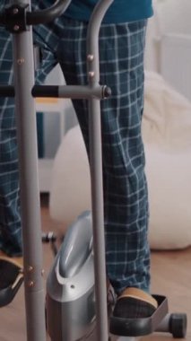 Dikey video: Evde statik bisiklet üzerinde bisiklet egzersizi yapan yaşlı adamın yakın çekimi. Sağlık ve dayanıklılık için stabil bisikletiyle kıdemli kişi eğitimi. Bisiklet kardiyo makinesi kullanarak emekli oldu.