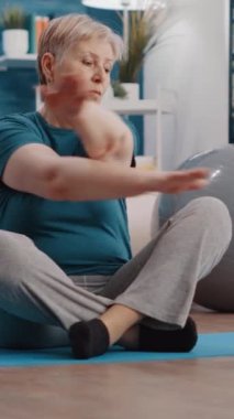 Dikey video: Üst düzey kadın laptopta online eğitim videosuna bakıyor ve yoga minderinde otururken jimnastik yapıyor. Emekli yetişkinler spor dersini bilgisayarda spor aktivitesi için izliyor..