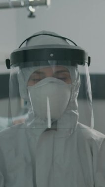 Dikey video: Koronavirüs salgınına karşı koruyucu giysili kadın portresi. Bulaşıcı enfeksiyonlu virüslü bölgede tehlikeli madde üniforması giyen sağlık görevlilerine yakın durun..