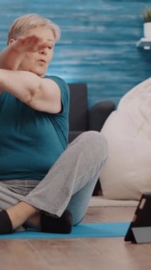 Dikey video: Yaşlı kadın egzersiz yapmak ve fiziksel aktivite yapmak için tablet eğitimi alıyor. Yaşlılar sağlık ve sağlık eğitimi için online egzersiz videosunu takip ediyor. Emekli