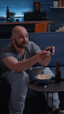 Dikey video: Kanepede oturmuş video oyunu oynayan kararlı heyecanlı adam, mutluluk çığlığı online yarışmanın tadını çıkarıyor. Oyun kontrol kumandası kullanan rekabetçi bir oyun kurucu.