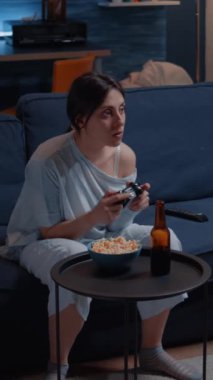 Dikey video: Oyuncu, oturma odasında kanepede oturan joystick ile oyun oynuyor ve yarışmayı kazanıyor. Heyecanlı kararlı kadın oyun konsolu playstation oyunu kullanıyor