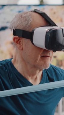 Dikey video: Emeklinin direniş bandını çekerken vr gözlükleri kullanarak antrenman yaparken elde çekilmiş görüntüleri. Yaşlı adamın elastik kemerle egzersiz yaptığı ve sanal gerçeklik giydiği yakın plan.