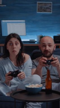 Dikey video: Video oyunu kazanan heyecanlı çift, koltukta otururken birbirlerine sarıldılar, mutluluk çığlıkları online yarışmanın keyfini çıkarıyorlardı. Playstation kullanan rekabetçi oyuncular