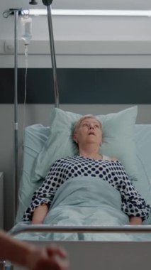 Dikey video: Doktor ve hemşire hastane koğuşunda solunum problemi olan yaşlı hasta için oksijen tüpü maskesi kullanıyor. Yatakta nefes nefese olan hasta kadını tedavi eden uzmanlar.