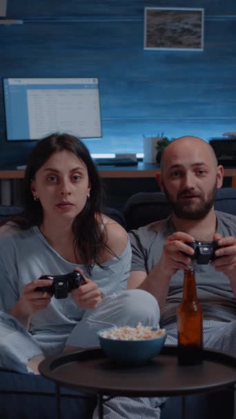垂直视频 有重点的一对夫妇在深夜玩电子游戏 专注于赢得在线比赛 让游戏玩家坐在沙发上 用控制杆一起玩电子游戏 — 图库视频影像