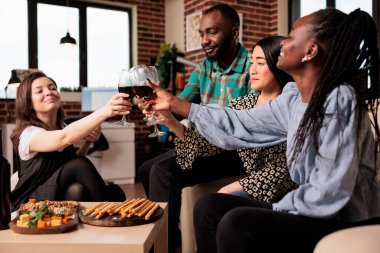 Farklı etnik kökenli arkadaşlar grubu, kadeh kaldırma, şarap içme, abur cubur yeme, genç yetişkin doğum günü partisinde eğlenme. Çok kültürlü insanlar arkadaşlığın tadını çıkarıyor..