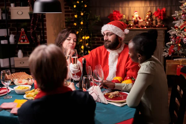 人们庆祝圣诞节 在节日桌上碰碰闪闪发光的酒杯 身穿圣爪服装的男人提议举杯 寒假庆祝活动 与大家庭团聚 — 图库照片