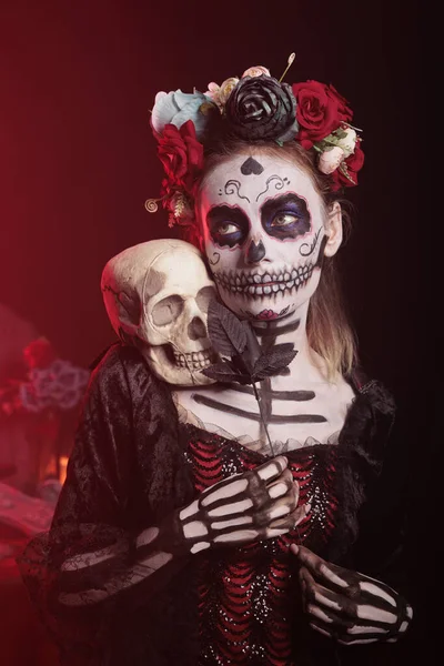 スタジオで頭蓋骨と黒いバラを保持し メキシコの休日を祝うために伝統的なメイクを身に着けている若い大人 聖ディオス ムエルトスのサンタ ムエルテや死の女神のように見える — ストック写真