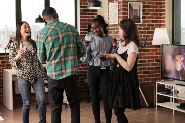 Happy diverse people laughing, smiling, dancing, having fun at multicultural friends, mates, gathering, party, reunion. Multiethnic partners drinking wine at coworkers meeting.