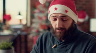 Kış tatilinde dizüstü bilgisayarda çalışan yeni yetme çalışanlar, noel ağacı süslemeleri ile ofiste rapor vermeyi planlıyorlar. Genç adam Noel Baba şapkası takıyor ve şenliği kutluyor. Kapatın. El kamerasıyla..