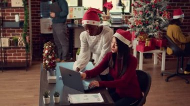 Noel tatili sezonunda süslü ofiste dizüstü bilgisayarda çalışan çeşitli çalışanlar. Araştırma planı üzerinde takım çalışması yapan kadınlar, xmas dekorasyonlarıyla uzayda şenlik yapıyorlar..