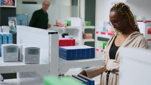 アフリカ系アメリカ人女性がビタミンリーフレットを読み 薬局の棚から薬のパッケージをチェックする ドラッグストアで薬や薬を買うための医薬品を見て — ストック動画