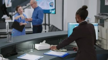 Bir kadın sağlık kontrolü randevu formlarını doldurmak için sabit hat telefonu kullanıyor ve resepsiyondaki sağlık sigortası belgelerini rapor ediyor. Telefon görüşmesinde konuşmak ve kayıt işlemlerine yardım etmek..