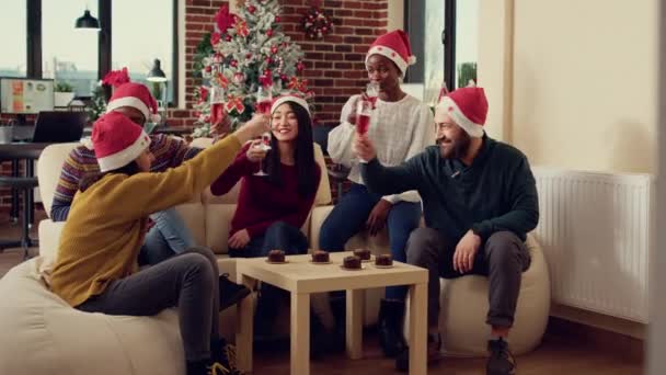 在办公室聚会上 一群多种族的人在酒杯上叮当作响 坐在沙发上 用酒精为庆祝圣诞节而敬酒 圣诞佳节喝含酒精饮料 — 图库视频影像