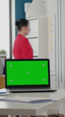 Dikey video: Ofisteki laptopta yeşil ekranı kapat. İzole edilmiş krom anahtar şablonuna sahip bilgisayar ve kopyalama alanı arkaplanı, iş alanında boş ekran. Kromakey uygulaması