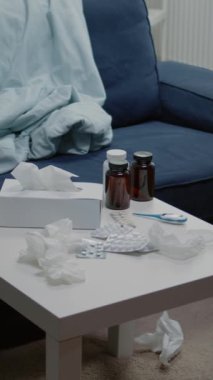 Dikey video: İlaç ve termometreyi odada kimse olmadan sehpanın üzerine kapatın. Gribe karşı ilaç, ilaç şişeleri, ilaç, ilaç, çay ve mendil olan boş bir yer