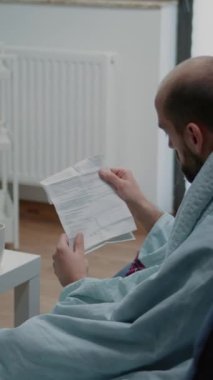 Dikey video: Grip semptomlarına karşı ilaç hakkında bilgi içeren migren okuma kağıdı olan yetişkin videosu. Baş ağrısı olan hasta bir adam soğuk algınlığını tedavi etmek için ilaç ve reçeteli tedavi broşürü tutuyor.