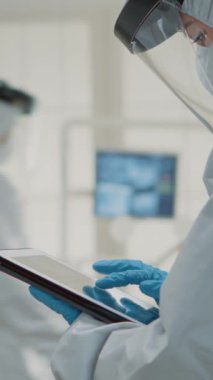 Dikey video: Diş asistanı, arka plandaki diş hekimine danışmanlık yaparken oral sağlık kliniğinde dijital cihazın diş röntgenini inceliyor. Ortodontist takımı modern teknolojiyle çalışıyor.