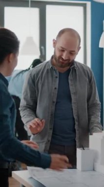 Dikey video: Bir grup iş arkadaşı inşaat düzenini tasarlamak için ilham kaynağı olarak bina modelini kullanıyor. Erkek ve kadın, Mac 'le birlikte planlar ve şehir yapısını planlamak için çalışıyor. Mimari proje