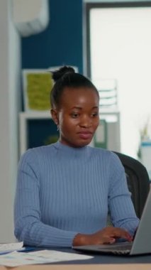 African american woman taking a break from work using laptop to drink a sip of coffee or tea from cup in busy office. Casual startup employee working relaxed with statistics in business workplace.