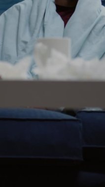 Dikey video: Başı ağrıyan ve hasta hisseden bir adama yakın çekim. Virüs belirtileri ve sağlık sorunları varken battaniyeye sarılmış migren ovalayan tapınakları olan bir kişi..