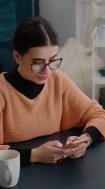 Dikey video: Üniversite öğrencisi online okul ödevi için yeniden seacrh yapmak üzere akıllı telefondan internete göz atıyor. Ders bilgisi ve bilgisi için cep telefonu kullanan ve not alan kadın.