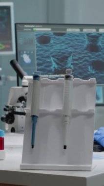 Dikey video: Laboratuvarda kimya teknolojisi olan bir kadın bilim adamı oturuyor. Pipetli biyokimya doktoru, kan emiciler, mikroskop, mikrobiyoloji deneyi için bilgisayarda daktilo.