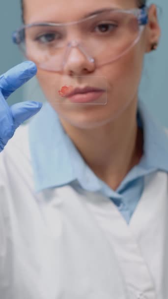 垂直ビデオ 科学研究室のガラストレイの血液検査を見て生物学の医師の閉鎖 科学者の女性のためのDnaサンプルを分析するクリニックでの保護のための眼鏡や手袋を着用 — ストック動画