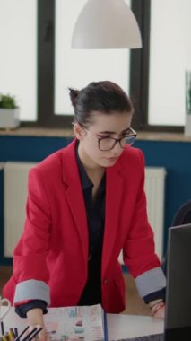 Dikey video: Proje yöneticisi kağıt ve bilgisayar istatistiklerine bakıyor, grafikler ve grafiklerle finansal analiz planlıyor. Şirket danışmanı iş büyümesi üzerinde çalışmak için veri araştırması kullanıyor.