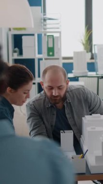 Dikey video: İş arkadaşları bina modelini inceledikten sonra plan tasarımı için takım çalışması yapıyor. Şehir geliştirme projesi için mimari yapı oluşturmak için maquette kullanan insanlardan oluşan bir ekip.