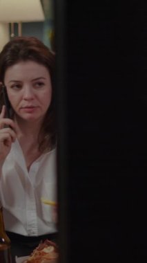 Dikey video: Sinirli kadın işten sonra patronuyla telefonda konuşurken paket servis kutularından yemek yemeye çalışıyor. Fast food yemeği olan biri iş için telefon kullanıyor.