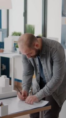 Dikey video: Erkek mimar bina yapısını ve modelini tasarlamak için planlar üzerine not alıyor. Endüstriyel müteahhit inşaat düzeni oluşturuyor ve Macquette ile proje stratejisi üzerinde çalışıyor..