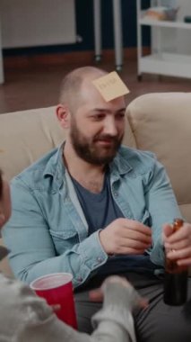 Dikey video: İş arkadaşlarının kapatılması işten sonra eğlenceli aktiviteler yapmak için yapışkan notlarla tahmin oyunu oynarlar. İş arkadaşları eğlenmek için içki ve atıştırmalık içerken sessiz sinema oynuyorlar..