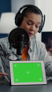 Dikey video: Stüdyoda etkili, yeşil ekranlı tablet üzerindeki ürünü tanıtıyor. Sosyal medya içerik yaratıcısı izole edilmiş arka plan ve kroma tuşlu dokunmatik ekran aygıtı öneriyor ve