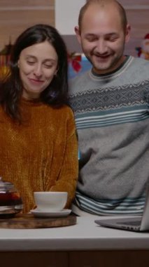 Dikey video: Noel arifesi kutlamaları için kutlama çifti video konferansında hediyeler veriyor. İnsanlar dizüstü bilgisayarda aileleriyle konuşuyor ve uzak mevsimsel kutlamalar için kamera önünde hediyelerini değiş tokuş ediyorlar..