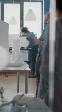 Dikey video: İnşaat geliştirme için model ve maquette ile planlar oluşturmak için cep telefonu kullanan mimar. Akıllı telefonla strateji projesini tasarlamak için çalışan insan mühendisi.