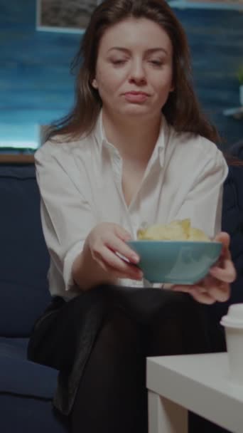 垂直视频 高加索女人坐在沙发上 一边看着相机一边吃碗里的薯片的肖像 带外卖食物的年轻人在客厅里吃饭 提包进餐的人 — 图库视频影像