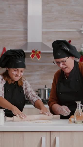垂直视频 祖父母享受寒假 而孙子孙女与围裙准备自制饼干甜点 用滚针做面团 厨房里装饰着圣诞装饰品 — 图库视频影像