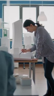 Dikey video: Kadın mimar, maketi ve maketi olan planlar tasarlıyor. Endüstriyel proje yaratmak için kağıt taslağı üzerinde inşaat planı planlayan mimar işçisi.