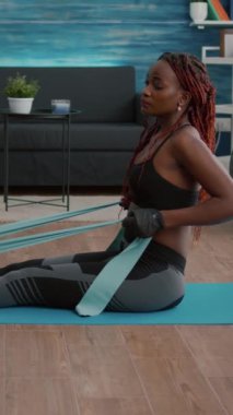 Verical video: Spor giyimli, spor giyinmiş, aerobik online spor antrenmanı izleyen, vücut kaslarını çalıştıran sağlıklı yaşam tarzının keyfini çıkaran estetik siyah bir kadın. Yoga haritasında oturan zayıf yetişkin