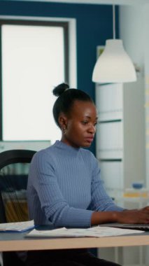 Portrait of smiling african american woman working on profit margin and sale statistics using laptop sitting at desk in busy startup office. Casual business employee happy with job result.