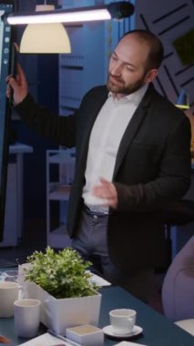 Dikey video: Odaklanmış adam lideri, şirket toplantı odasında gece geç saatlerde çalışan monitörle yönetim projesini açıklıyor. Çok çalışan çok ırklı takım çalışması şirketlerin beyin fırtınası