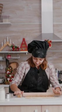 dikey video: Torun ev yapımı kurabiye hamuru yapıyor. Xmas dekore edilmiş mutfak masasında duran merdaneyle. Mutlu aile gülümseyerek selfie çekerken Noel tatilinin tadını çıkarıyor.