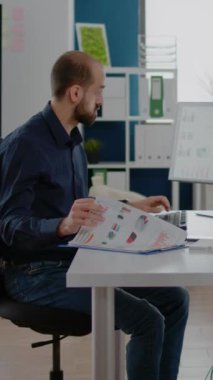 Dikey video: İş adamı pazarlama stratejisi için çizelge ve bilgisayar kullanıyor. Analiz ve geliştirme için araştırma verileri üzerinde çalışan kurumsal bir işi olan girişimci. Projesi olan adam