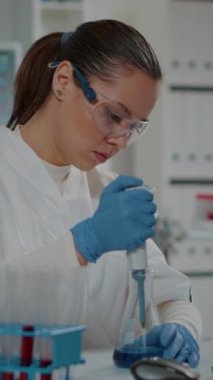 Dikey video: Laboratuvar çalışanı kimyasal yenilikler için deney tüpleri ve deney tüpleriyle mikro pipet kullanıyor. Mikrobiyoloji analizi için laboratuvar ekipmanlarıyla çalışan bir mühendis..