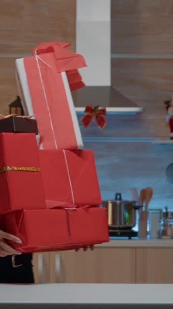 垂直ビデオ クリスマスの前夜のお祝いのために設計されたキッチンカウンターにプレゼントを置くお祭りの女性 友達や家族へのプレゼント付きの箱を自宅で準備する陽気な若い人 — ストック動画