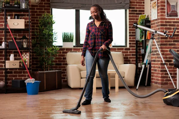 Independent woman takes care of spring cleaning, vacuums the dust in the living room floor at home. Housewife in slippers does home chores with dedication, tidies and cleans the whole place.